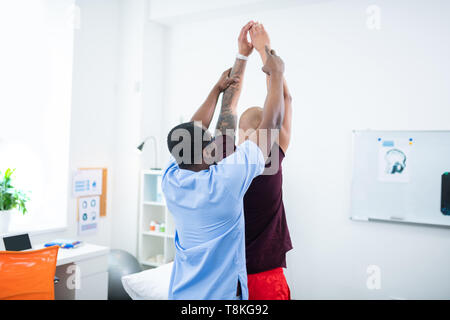 Dark-skinned therapist raising hands of sportsman coming to him Stock Photo