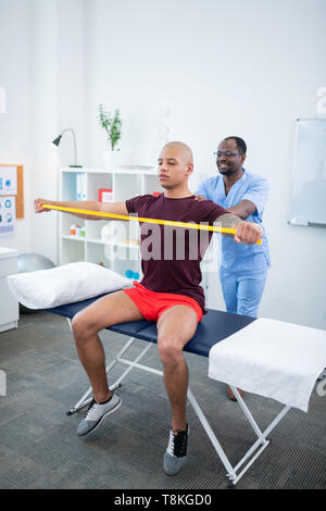 Therapist smiling while watching his patient doing exercises Stock Photo