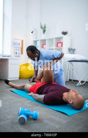 Bald sportsman lying on mat and having physical therapy for legs Stock Photo