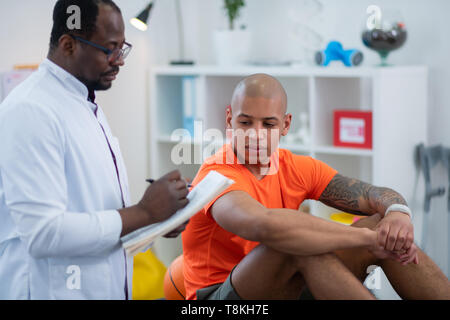 Tattooed sportsman listening to his doctor after getting injury Stock Photo
