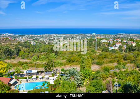 Amazing view of subtropical landscape in Cypriot Kyrenia region taken in summer season. The countryside buildings surrounded by green trees are overlooking the Mediterranean sea. Stock Photo
