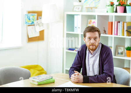 Calm bearded man sitting in a classroom and waiting for his students Stock Photo