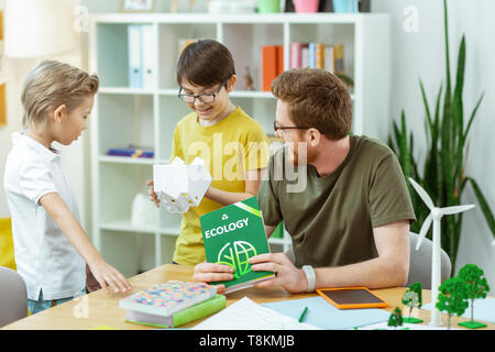 Smiling dark-haired boy inspecting plastic house during lesson Stock Photo
