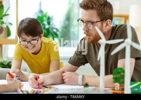 Smiling dark-haired boy being interested in cognitive project Stock Photo