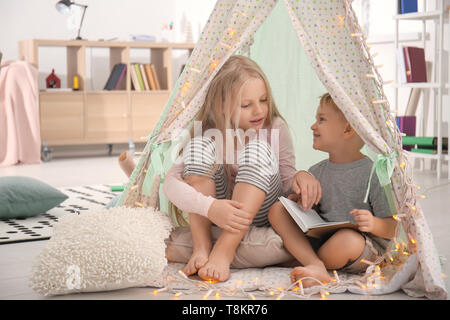 Cute little children with book sitting in hovel at home Stock Photo