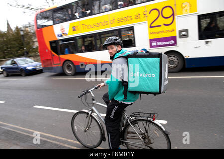 Oxford, United Kingdom - Mar 3, 3017: Rear view of young male cyclist delivering food fast to client via Deliveroo App - commuting fast in the university city with big thermo bag with Deliveroo logo Stock Photo