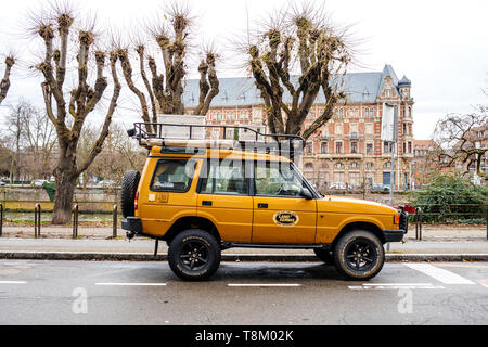 Strasbourg, France - Dec 27, 2017: Side view of new vintage yellow Land Rover Defender Camel Trophy with luggage on the roof parked in central city street with Stock Photo