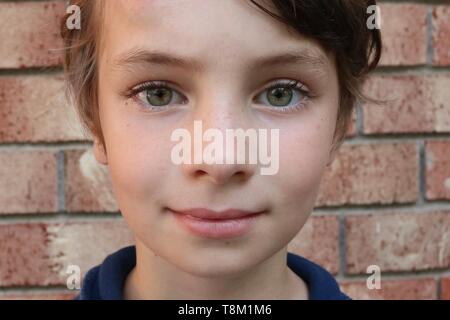 Portrait of a child with big green eyes in front of a brick wall