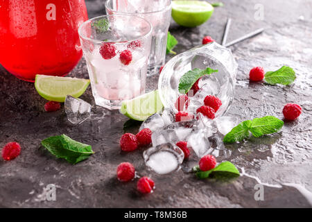 Glasses with ice cubes, raspberries and lime on grey table Stock Photo