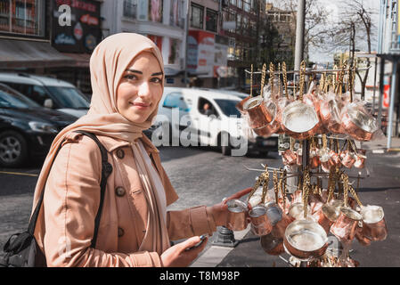 Beautiful Muslim women in headscarf and fashionable modern trendy clothes buys copper Turkish coffee pots.Muslim women lifestyle travel tourist concep Stock Photo