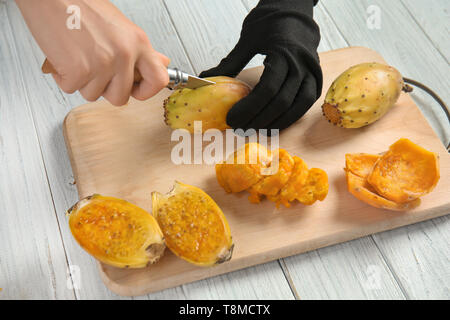 Woman cutting ripe cactus pear on wooden board Stock Photo