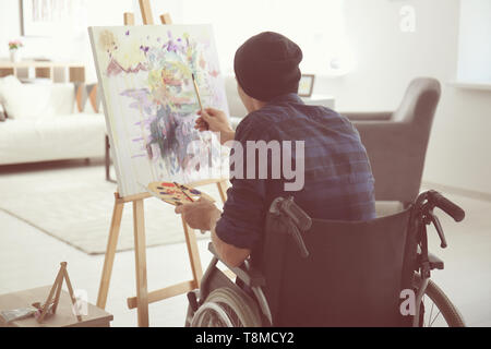 Young artist in wheelchair painting picture at home Stock Photo