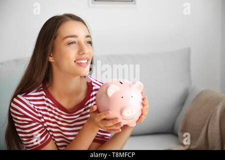 Young woman with piggy bank at home Stock Photo