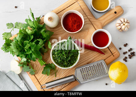 Cooking background. Raw ingredients for preparation Argentinian green Chimichurri or Chimmichurri salsa or sauce on white wooden table Stock Photo