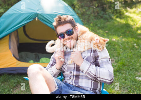 People, tourism and nature concept - Man in sunglasses holding cat on shoulders Stock Photo