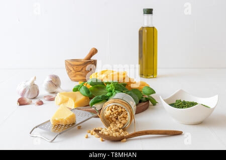 Making pesto. The table with ingredients to produce basil pesto. Mortar, fresh basil herbs, pine nuts, olive oil, parmesan cheese, garlic, bowl with p Stock Photo