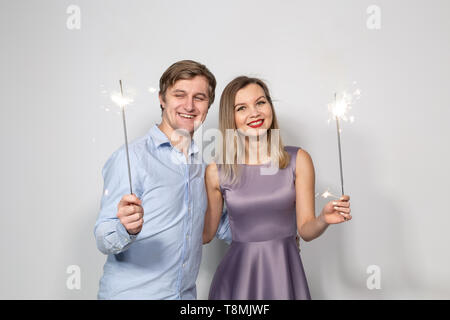 Party, celebration, event and holidays concept - man dressed in blue shirt and woman dressed in purple dress hold a firework stick Stock Photo