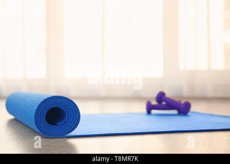 Yoga mat with dumbbells on light floor Stock Photo