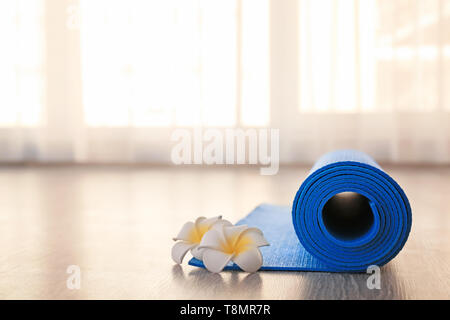 Rolled yoga mat and flowers on floor Stock Photo