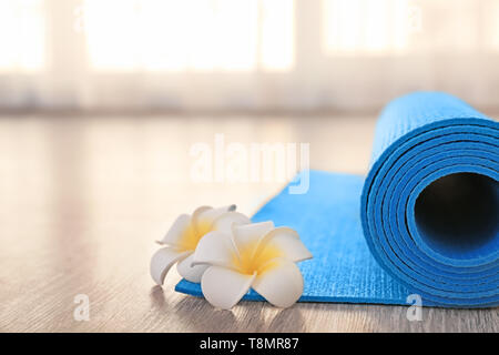 Rolled yoga mat and flowers on floor Stock Photo