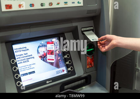 Abu Dhabi, UAE - March 29. 2019. A man's hand picks up paper check from an ATM of Abu Dhabi Commercial Bank Stock Photo