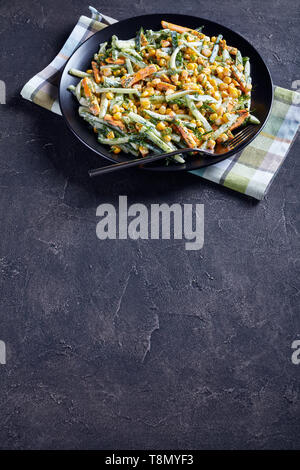 cucumber corn cheese salad with yogurt lemon dressing sprinkled with finely chopped dill on a black plate on a concrete table, vertical view from abov Stock Photo