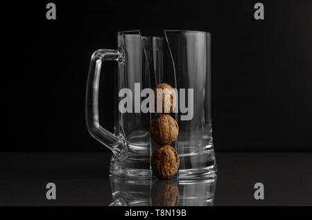 cracked beer mug with three walnuts on a dark background Stock Photo