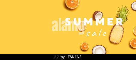 Creative summer composition of tropical fruit juices on a yellow background: oranges, coconuts, lemons, pineapples. Stock Photo