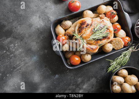 Roasted chicken with potatoes, tomatoes with sauces and wine on black table. Stock Photo