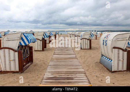 Colorful striped wooden hooded beach chairs (strandkorb) on a sandy Baltic beach in Travemunde seaside resort near Luebeck city, Germany Stock Photo