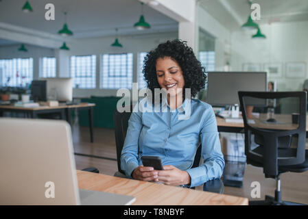Smiling businesswoman sitting at her desk reading a text message Stock Photo