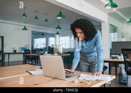 Focused young businesswoman standing at her desk using a laptop Stock Photo