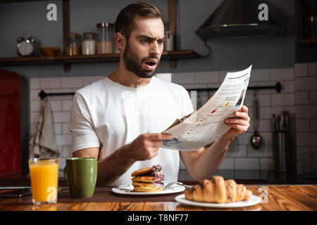 Angry shocked man having breakfast, reading newspaper Stock Photo