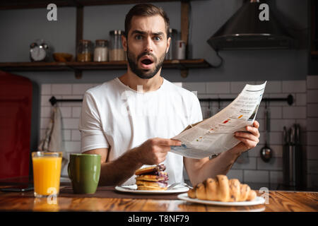 Angry shocked man having breakfast, reading newspaper Stock Photo