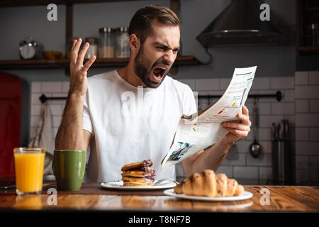 Angry shocked man having breakfast, reading newspaper Stock Photo