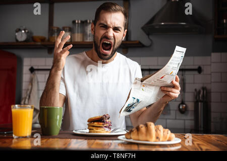 Angry shocked man having breakfast, reading newspaper Stock Photo