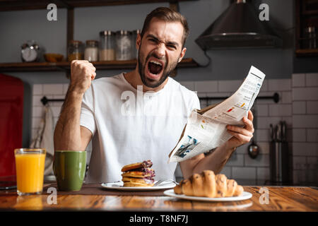 Angry shocked man having breakfast, reading newspaper Stock Photo