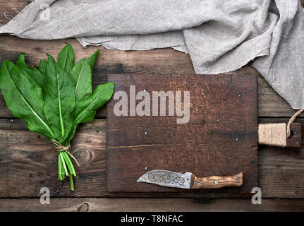 bunch of fresh green sorrel leaves and old brown cutting board on a wooden table, top view Stock Photo