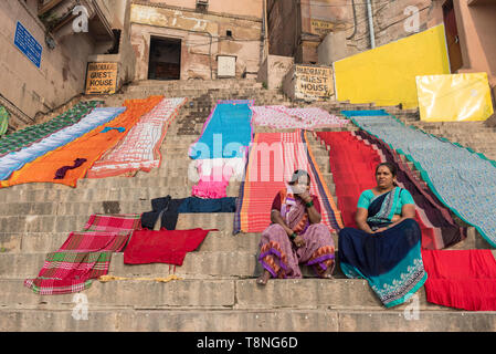 Two women and coulourful fabrics drying in the sun on  steps (ghats) of the River Ganges, Varanasi, India Stock Photo