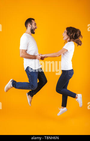 Full length photo of happy couple laughing and holding hands isolated over yellow background Stock Photo