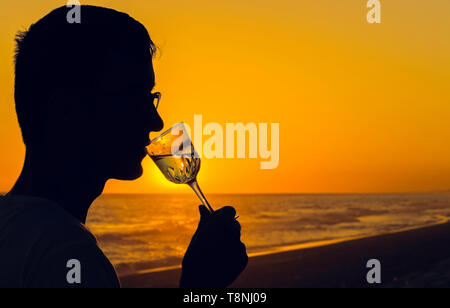 Silhouettes of Man drink glasses of champagne wine at sunset dramatic yellow sky. Empty Copy space for inscription Stock Photo