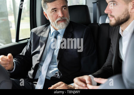 business colleagues discussing business ideas while sitting in backseat of the car or taxi. Stock Photo