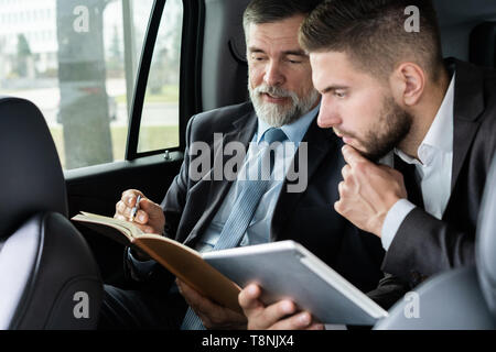 business colleagues discussing business ideas while sitting in backseat of the car or taxi. Stock Photo