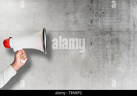 hand holding red and white megaphone against rough concrete wall Stock Photo
