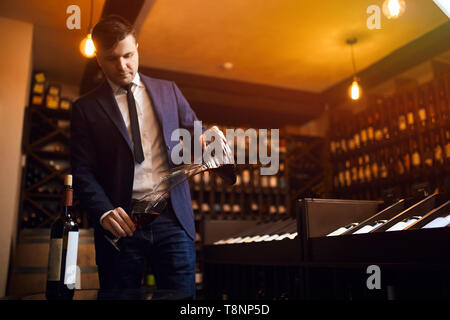 stylish young man in blue suit and white shirt pouring wine from decanter to the glass. close up photo.copy space. passion for wine Stock Photo