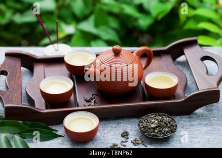 Green tea in tea pot and bowls, cups on a wooden tray. Outdoor background. Stock Photo
