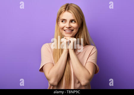 happy cunning girl with fists on chin, and dreams or thinks.close up photo. I have a great idea. blonde woman in beige T-shirt looking aside.positive girl looking forward somebody Stock Photo