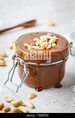 Homemade salted caramel with nuts in a glass jar. Ingredient for cake snickers. Stock Photo