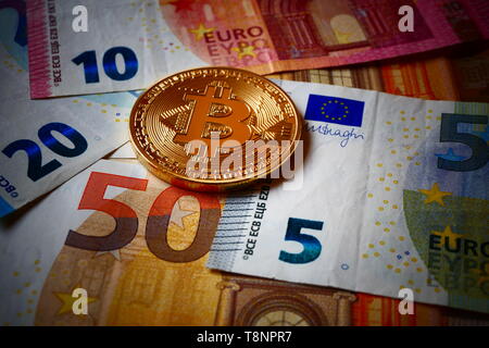 An golden Bitcoin, an virtual currency in physical coin form, displayed on Euro banknotes Stock Photo