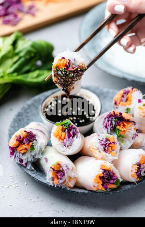 Rice paper rolls or fresh spring rolls stuffed with vegetables and shrimps. Person eating rolls, asian cuisine Stock Photo